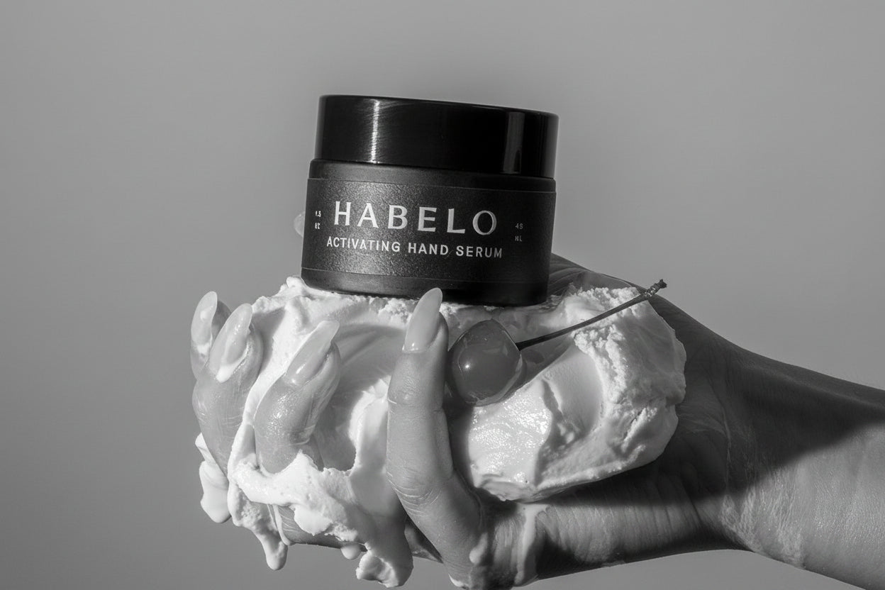 Hand holding a jar of Habelo hand serum with a cherry on top against a neutral background